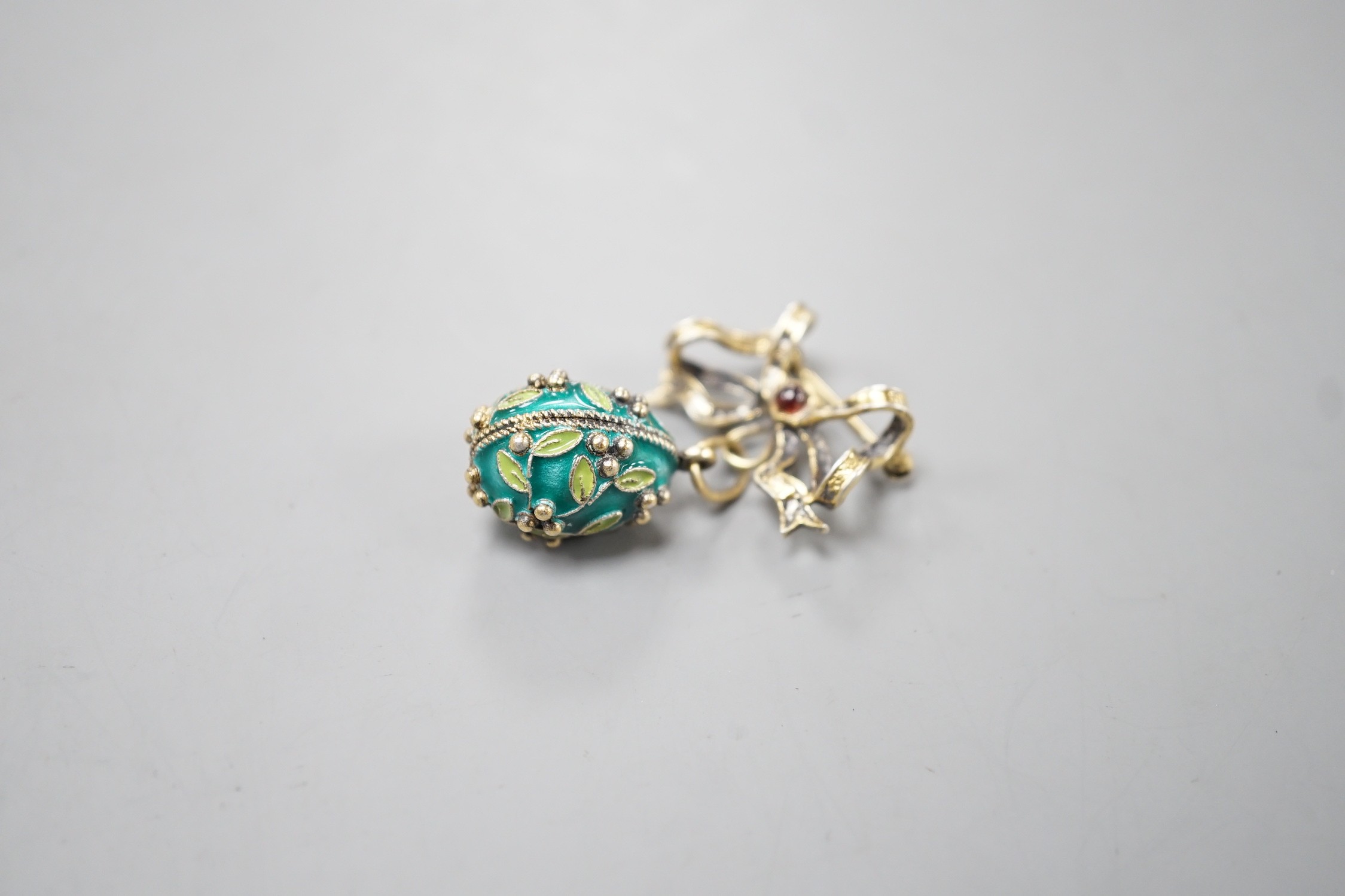 A mid 20th century Soviet gilt 925 and enamelled egg pendant, 21mm, on a gilt white metal ribbon bow suspension brooch.